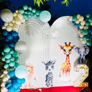 Jungle-themed birthday party setup with colorful balloon arch, animal cutouts, and LED number 2 on a red carpet