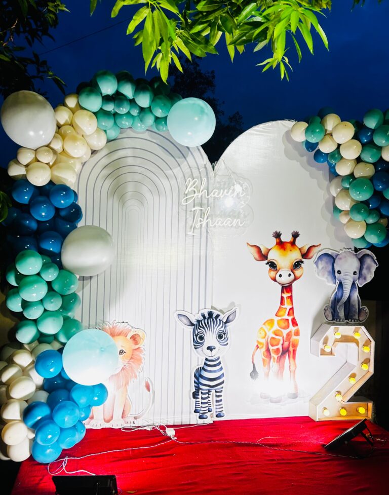 Jungle-themed birthday party setup with colorful balloon arch, animal cutouts, and LED number 2 on a red carpet