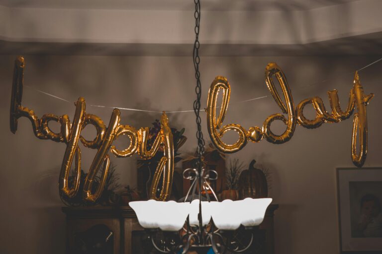 Festive gold balloons spelling 'happy bday' hang indoors, ideal for party themes.
