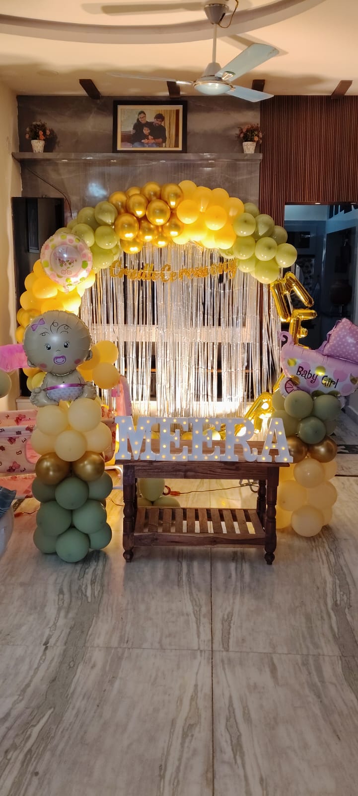 Luxury baby girl welcome balloon decoration with pastel yellow and sage green organic balloon arch, silver shimmer backdrop, LED name letters, baby girl foil balloons, and premium home welcome setup by Pushpaa Party Hub in Hyderabad."